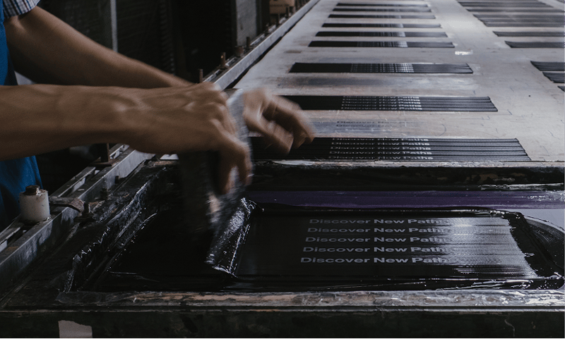 A Tasindo craftsperson screen-printing the “Discover New Paths” motif onto ZSA Backpack fabric panels.
