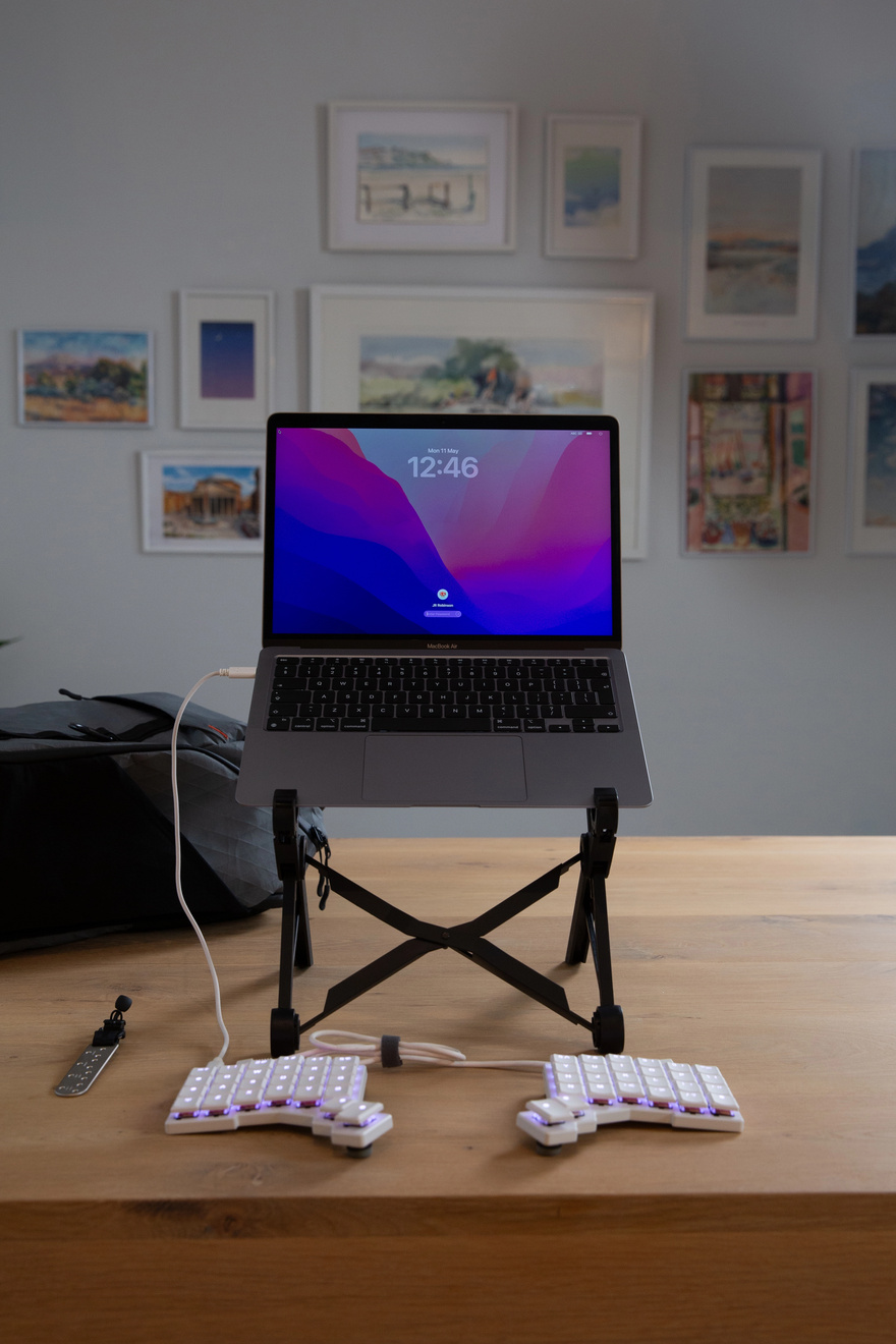 A full ergonomic workspace including a ZSA split keyboard and a laptop, all emerging from the ZSA Backpack.